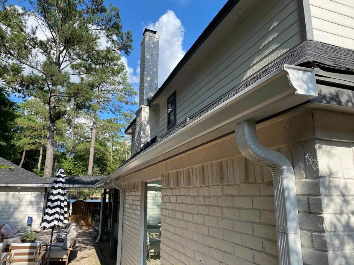 White gutter and downspout installation along a two-story roofline